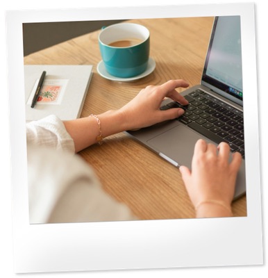 Person typing on a laptop with a teal coffee mug and notebook and pen nearby.