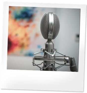 Silver tabletop microphone with an abstract colourful artwork in the background.