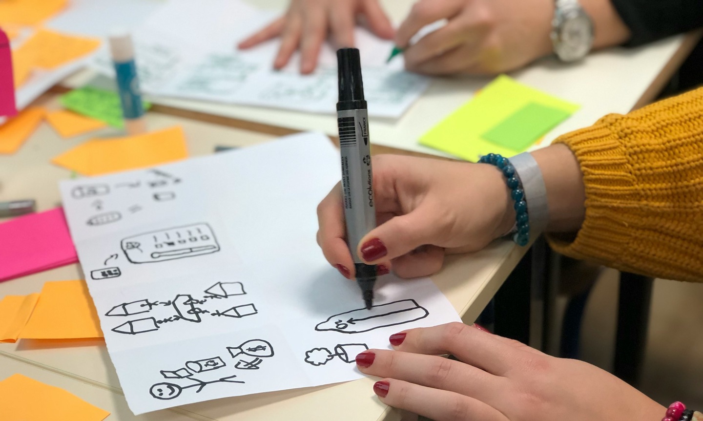 Drawing cartoons/diagrams with a black marker on white paper, with colourful sticky notes around the drawing surface.